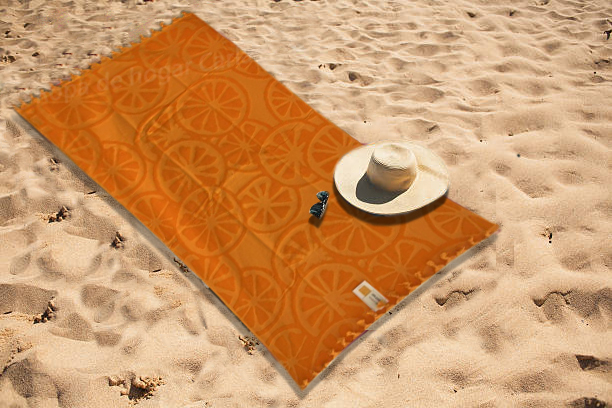Toalla naranja sobre arena con un sombrero blanco y un objeto azul junto a ella.