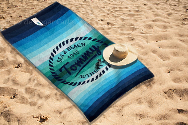 Toalla de playa azul con un sombrero sobre la arena.