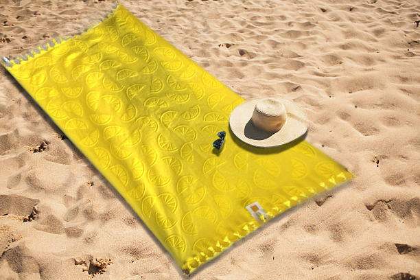 Toalla amarilla sobre arena, con un sombrero y unas gafas de sol.