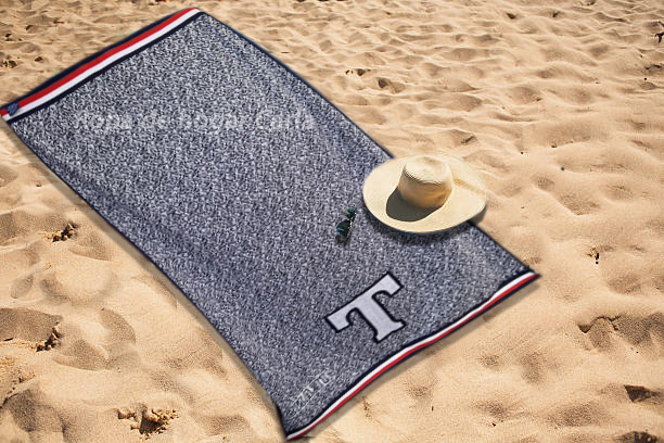 Toalla de playa con un sombrero sobre arena clara.