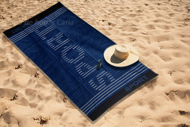 Toalla azul con la palabra "Sport" y un sombrero sobre la arena de la playa.