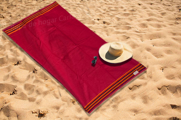Toalla roja en la arena con un sombrero y unas gafas de sol.