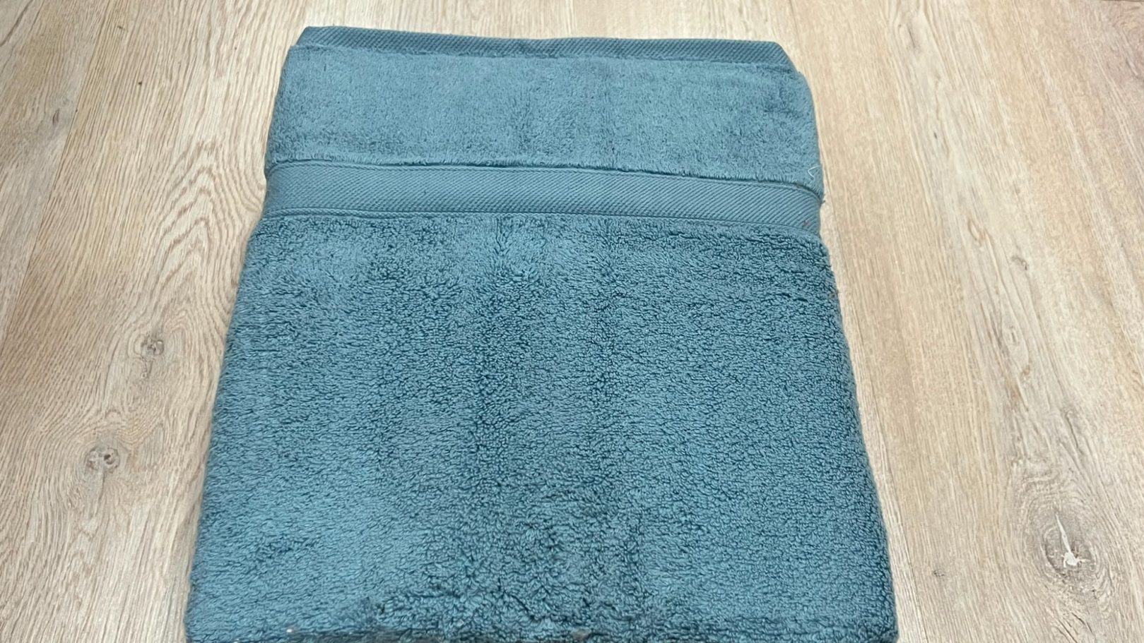 Toalla de color teal sobre un suelo de madera clara.