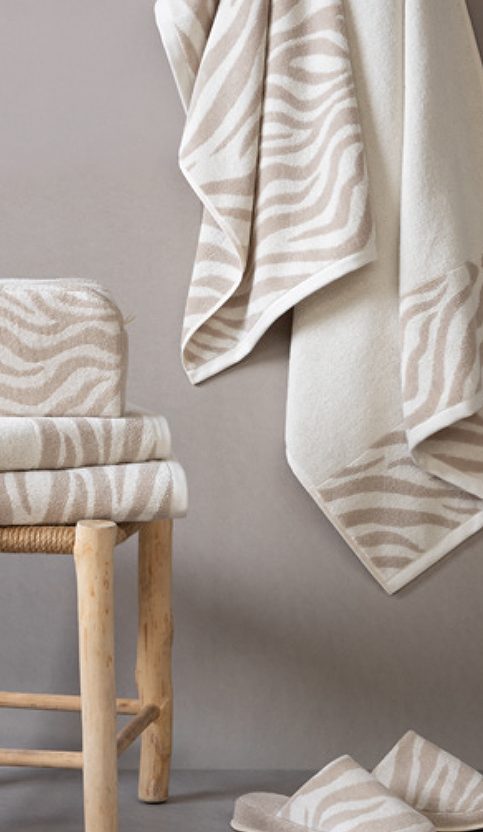 Toallas animal prime zebra softII Mantas y toallas de estilo zebra en tonos beige sobre una silla de madera.