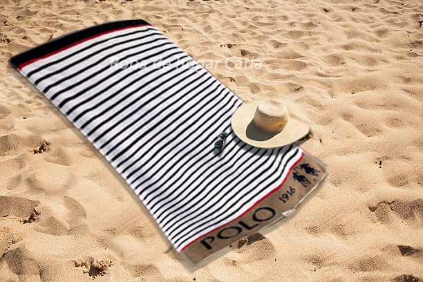 Toalla de rayas en la playa, con un sombrero y gafas de sol sobre la arena.