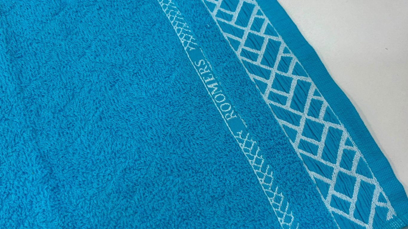 Toalla azul con borde blanco decorativo de diseño geométrico.