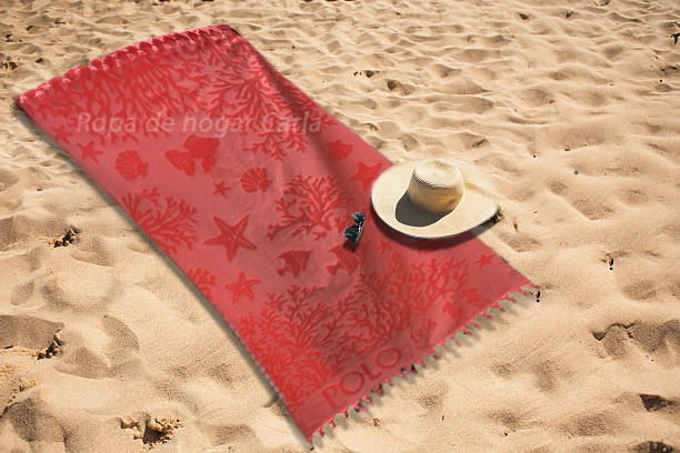 Toalla roja con estampado en la arena, acompañada de un sombrero y un pequeño objeto.