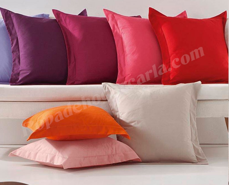 Cojines basicos Surtido de cojines en tonos morados, rosa, rojo, naranja y beige sobre un sofá blanco.