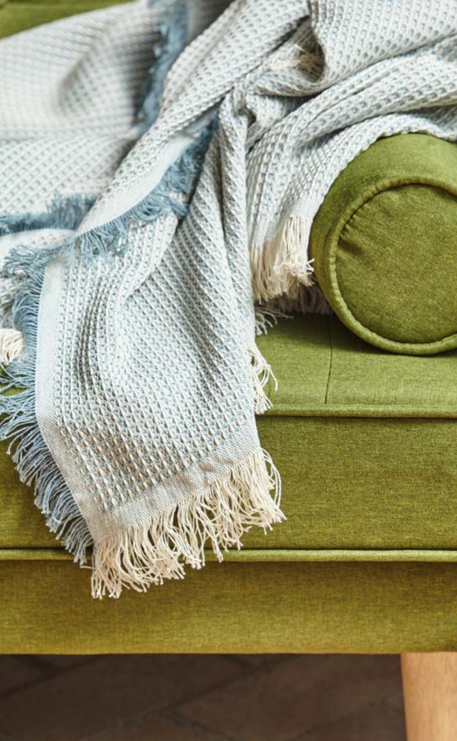 Multiusos de algodón Manta de color azul claro sobre un sofá verde con cojín.