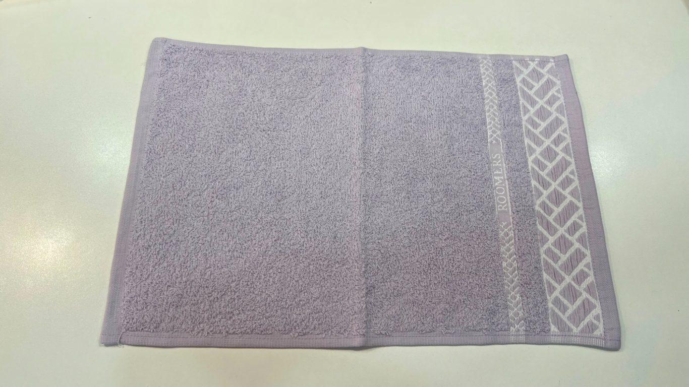 Toalla morada con un bordado decorativo en un lateral.