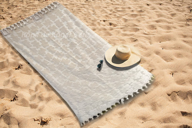 Manta blanca sobre la arena con un sombrero y gafas de sol.