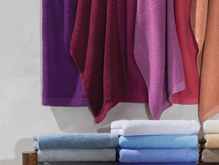 Toallas de algodón Lasa Pure Toallas de varios colores colgadas y apiladas en una superficie.