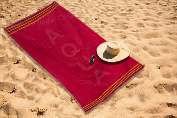 Toalla roja en la playa con un sombrero y unas gafas de sol sobre la arena.
