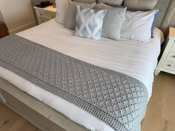 Cama con edredón gris y cojines decorativos en una habitación iluminada.