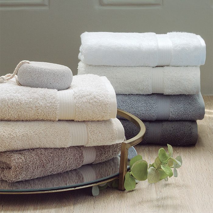 Toallas de algodón Lasa Pure Toallas de diferentes colores apiladas sobre una bandeja con decoración natural.