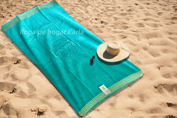 Toalla de playa azul sobre arena con un sombrero y unas gafas de sol al lado.