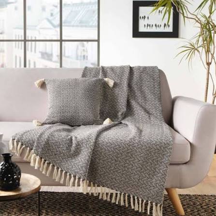 Manta con flecos y cojín decorativos sobre un sofá claro en un ambiente acogedor.