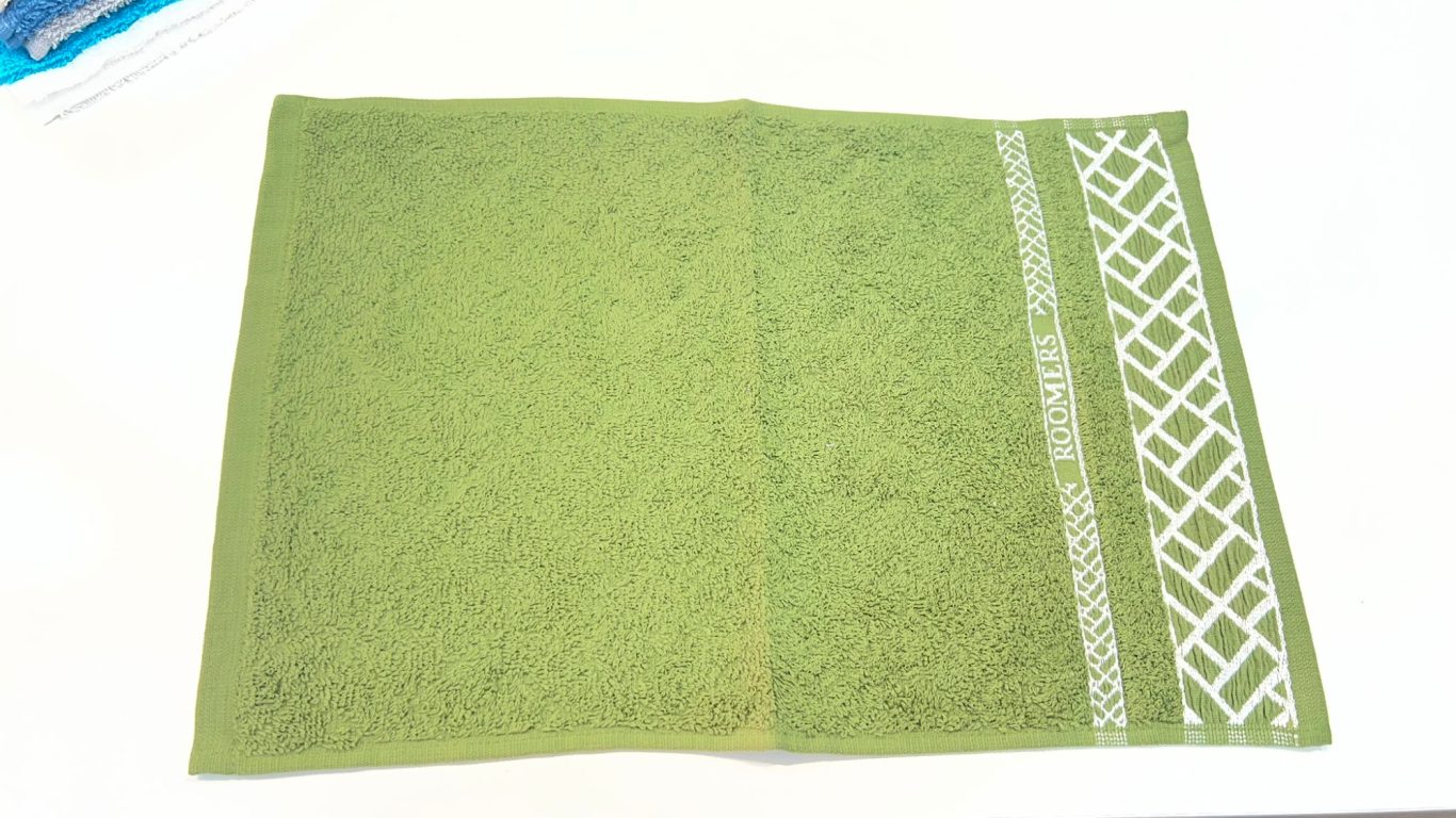 Toalla verde con diseño blanco en un lado y textura suave en toda su superficie.