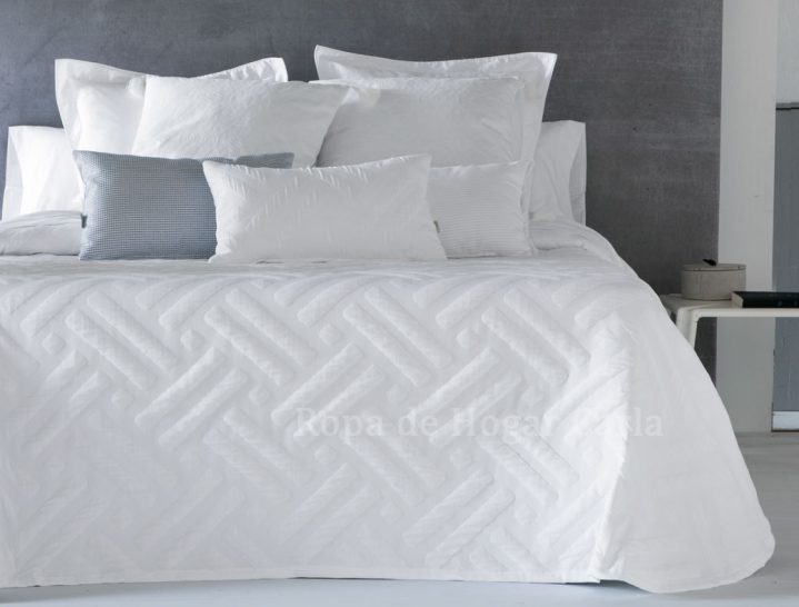 Juego de cama blanco con cojines decorativos en una cama moderna.