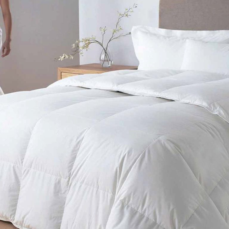 Edredón de cama blanco sobre una cama con almohadas y una mesita de noche.