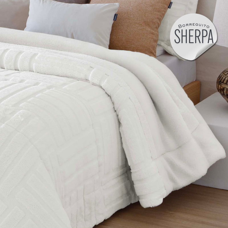 Funda de cama blanca de textura suave, acompañada de cojines marrones y grises.