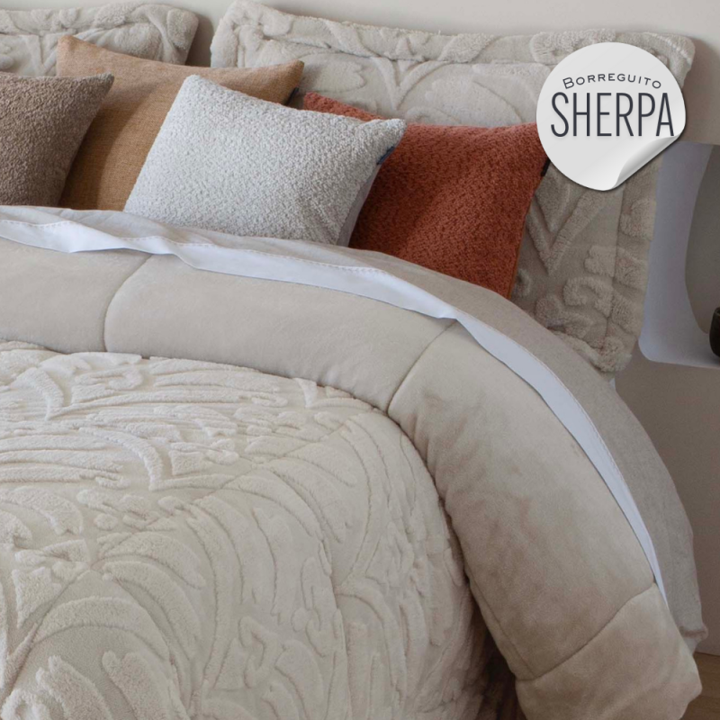 Cama con edredón beige y cojines en tonos neutros y terracota.