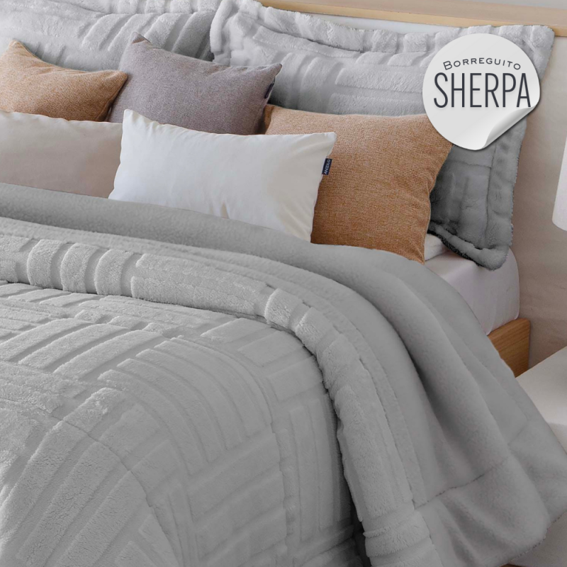 Colcha gris con almohadas en tonos neutros sobre una cama.