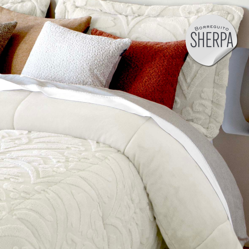 Colcha blanca con texturas, almohadas de colores cálidos y logo de Sherpa.